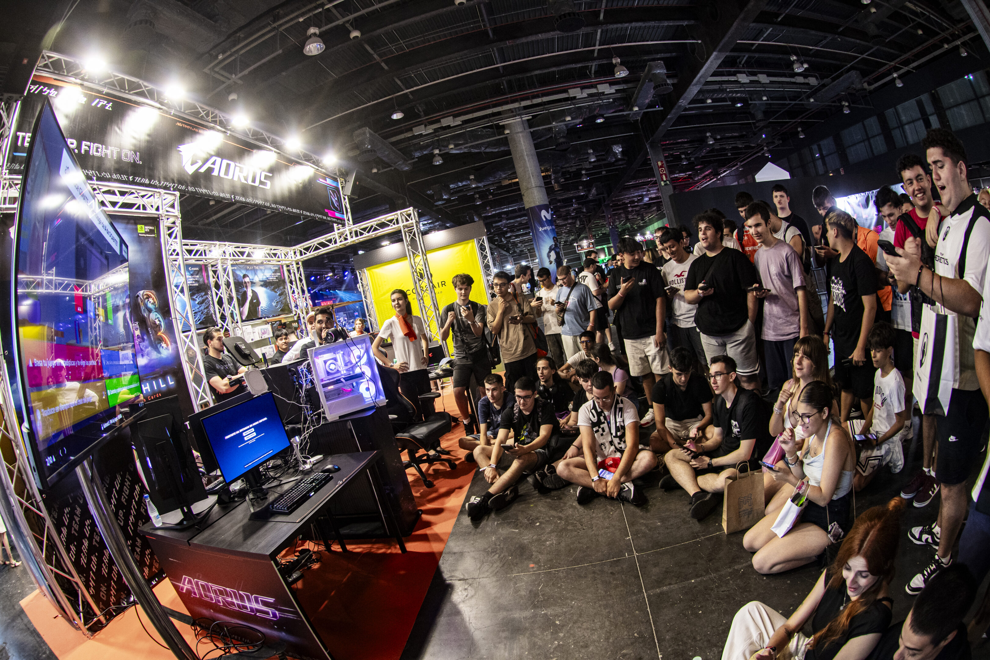 Fotografía de ojo de pez de un grupo de gente sentados en el stand de Aorus jugando a un kahoot